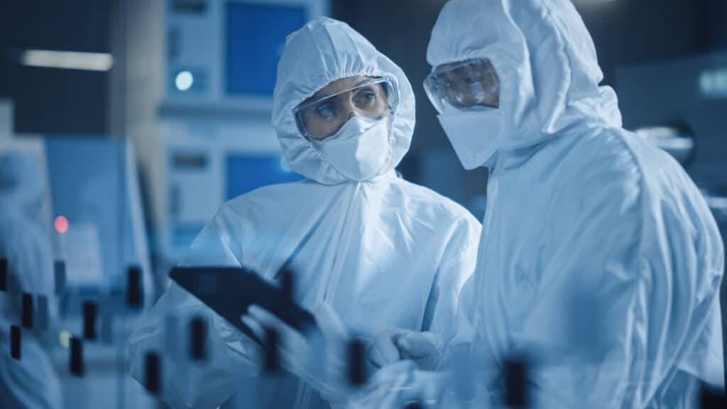 Clean room manufacturing workers in a controlled/clean manufacturing environment wearing protective garments and reviewing a tablet for quality assurance